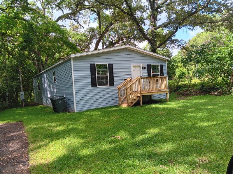 A mobile home with a deck and stairs is sitting on top of a lush green field.