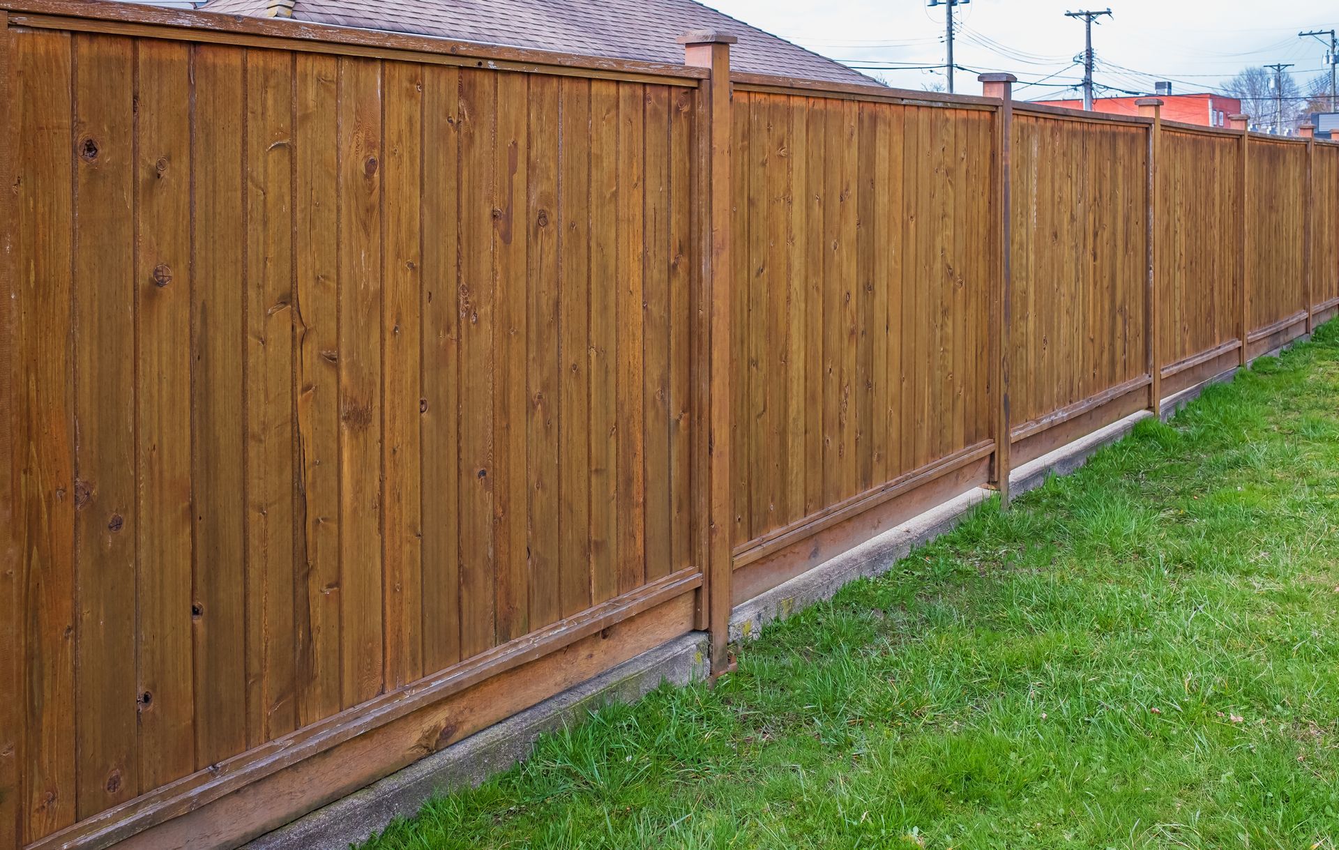 A wooden fence surrounds a lush green lawn in front of a house.