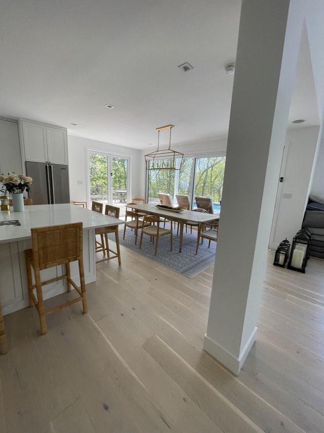 Bright modern dining room with wooden table, chairs, kitchen island, and large windows overlooking greenery