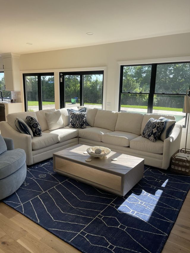 Bright living room with beige sectional, navy rug, and large windows overlooking a green yard