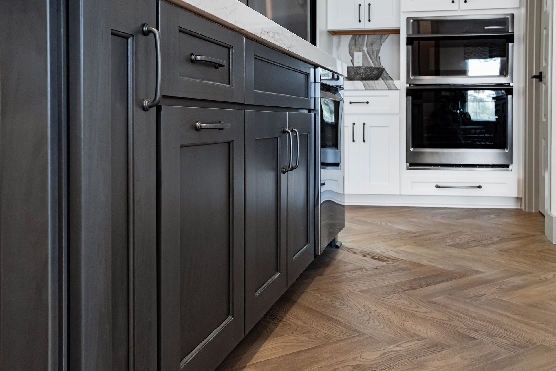 Gray kitchen cabinets with silver hardware and herringbone wood flooring.