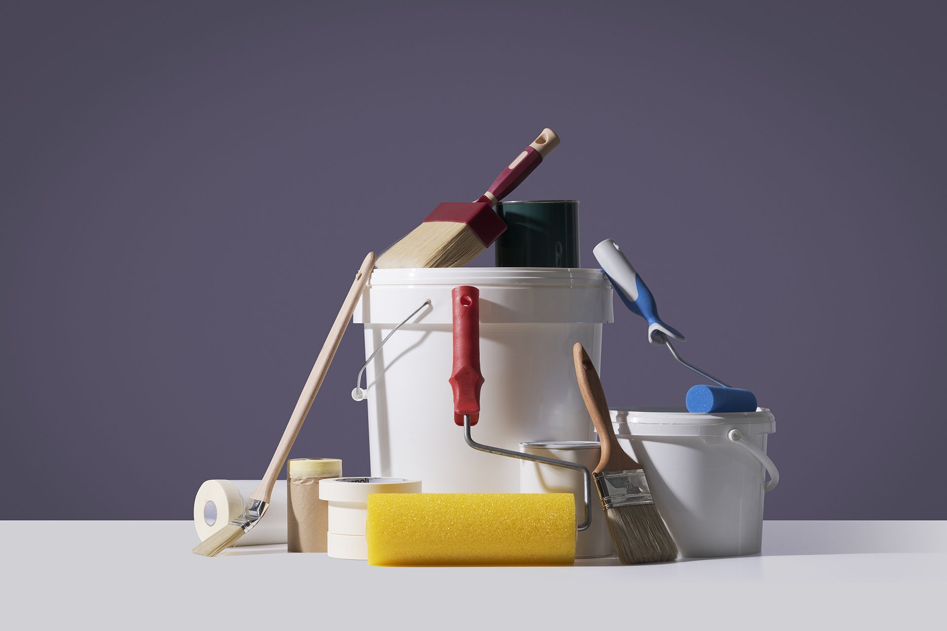 Paint supplies: buckets, rollers, brushes, and tape against a purple background.