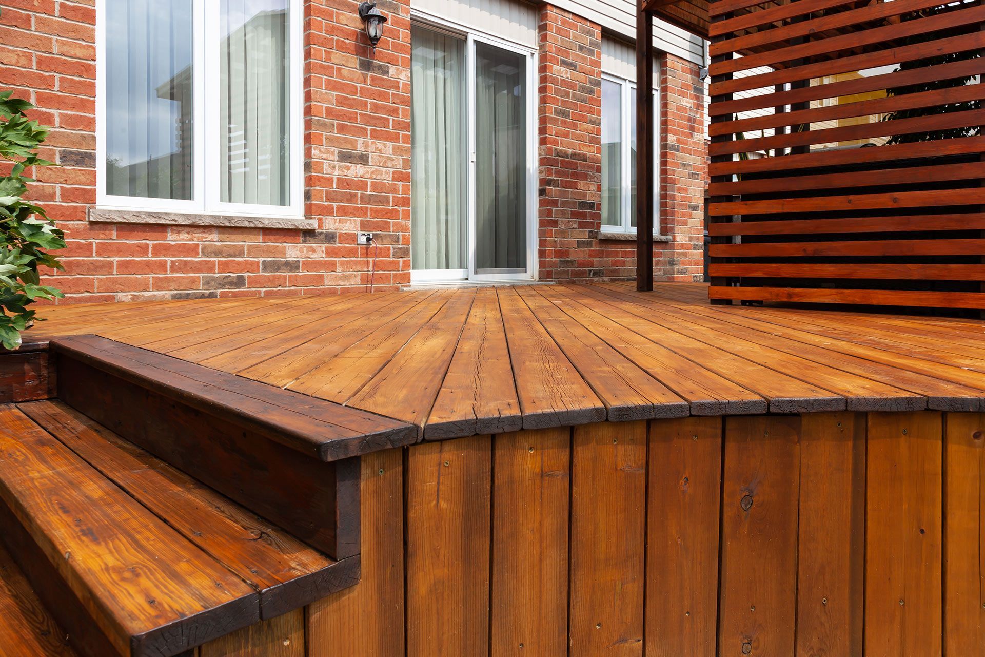 Wooden deck stained brown with steps, next to a brick building.