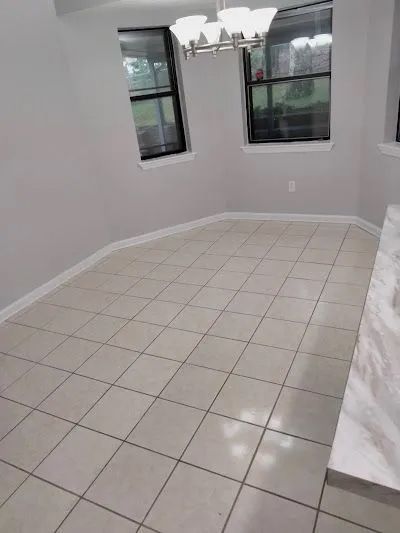 Empty dining area with tiled floor, two windows, and chandelier. Light gray walls and white trim.