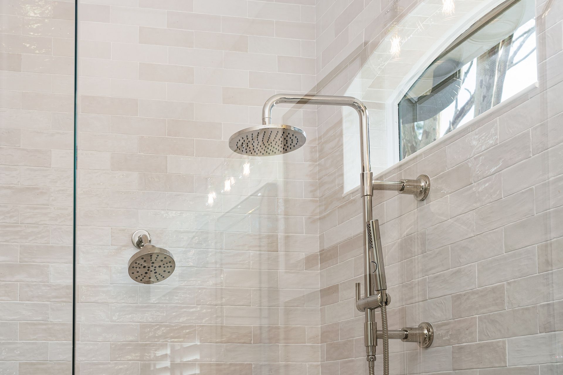 Shower with two showerheads, one overhead and one on the wall, against light-colored brick tile.