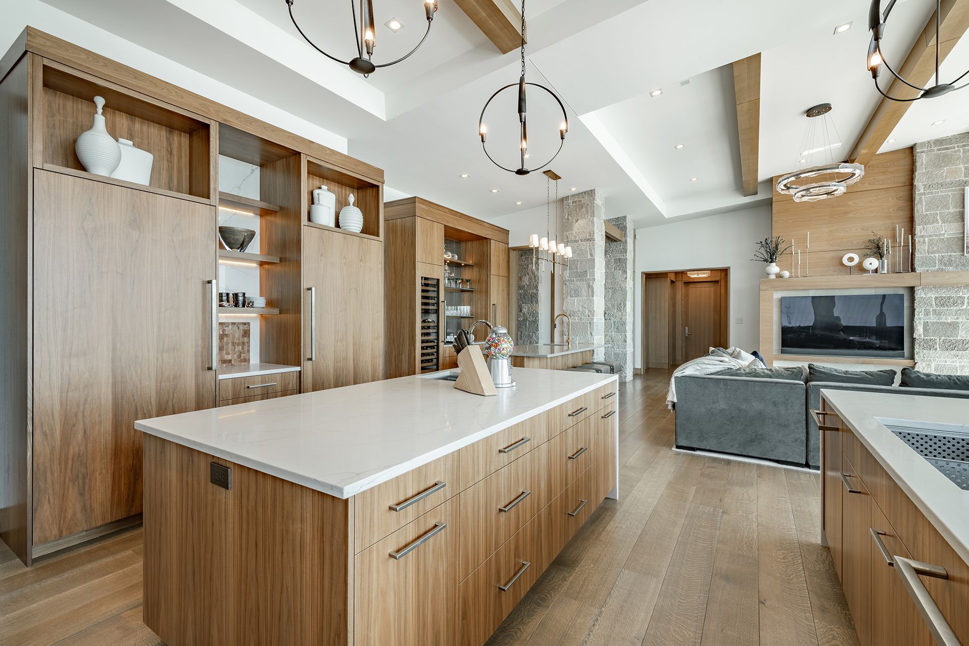 Modern kitchen with wooden cabinetry, white countertops, and an island. Open concept with a living area visible.