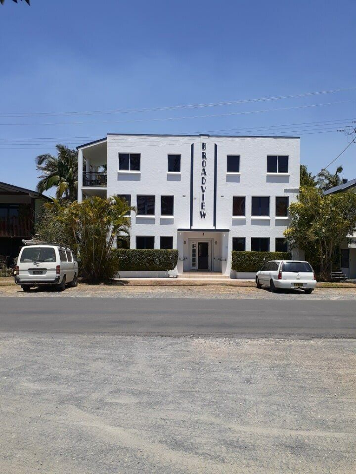Two Cars Are Parked In Front Of A Large White Building — Yves De Wilde Quality Painting Services In Lismore, NSW