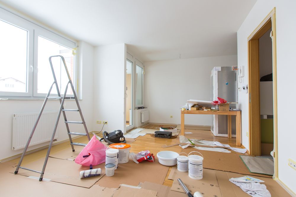 Room under renovation with paint supplies, ladder, and protection on the floor.
