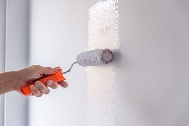 A Person Is Painting A Wall With A Paint Roller — Yves De Wilde Quality Painting Services In Lismore, NSW