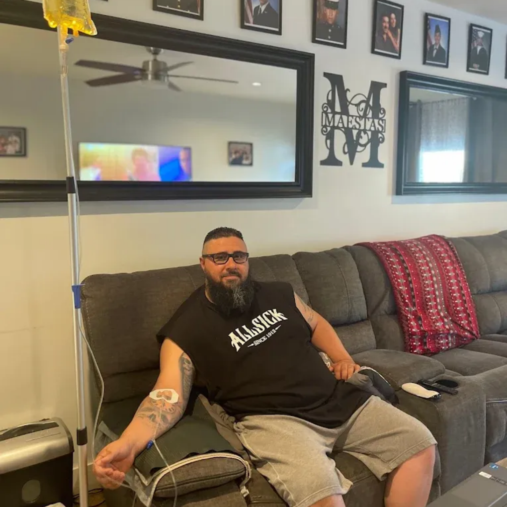 Man receiving IV drip while seated on a couch indoors.