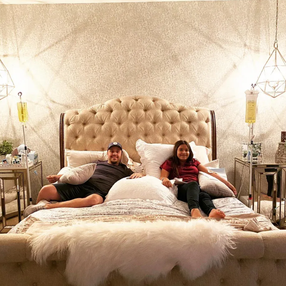 Man and girl on bed with IV drips. Luxurious room with decorative headboard and side tables.