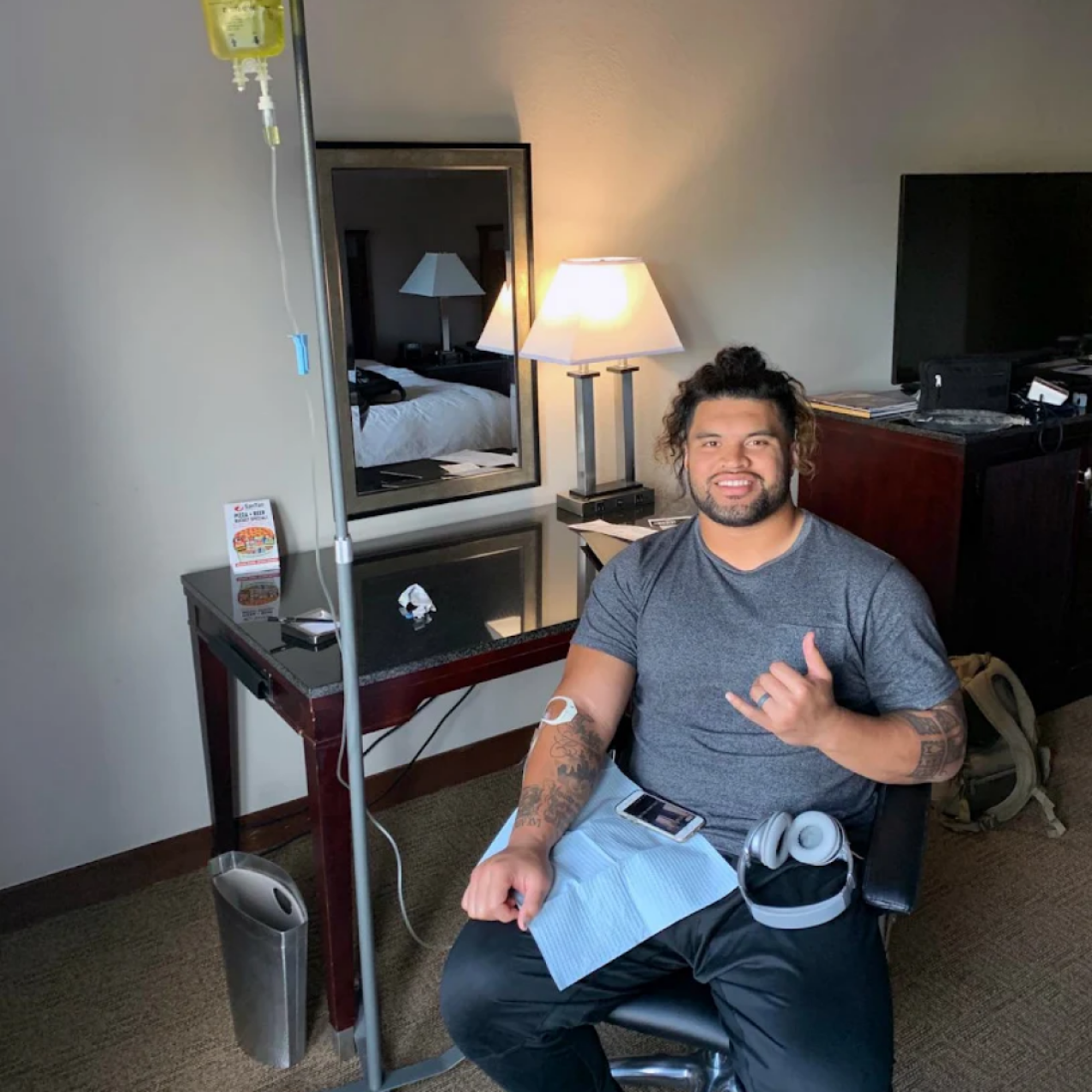 Man receiving IV treatment in a room, smiling and giving a shaka hand sign.