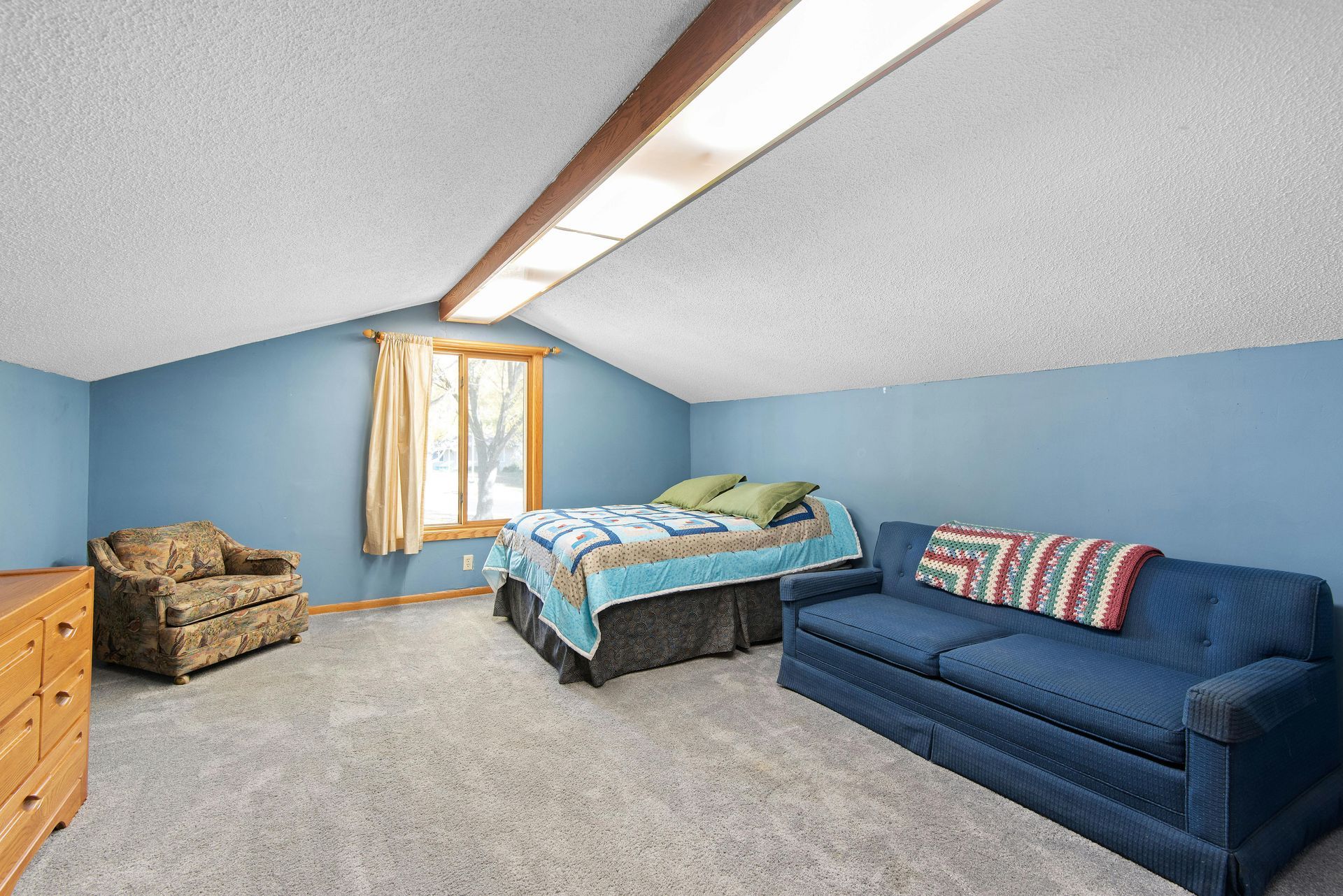 Bedroom with blue walls, carpet, bed, sofa, armchair, dresser, and window.