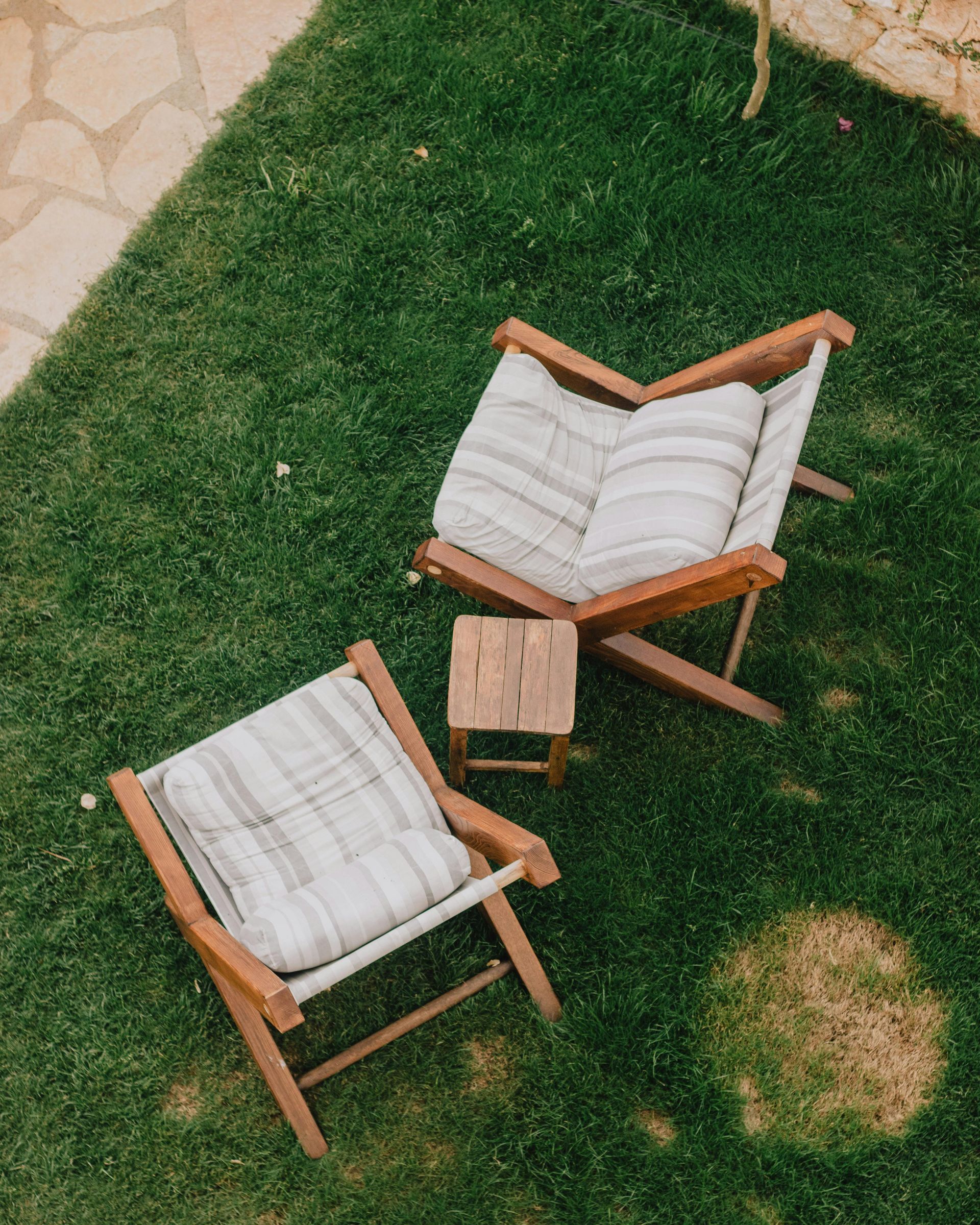 Two wooden chairs with striped cushions and small wooden table on grass.