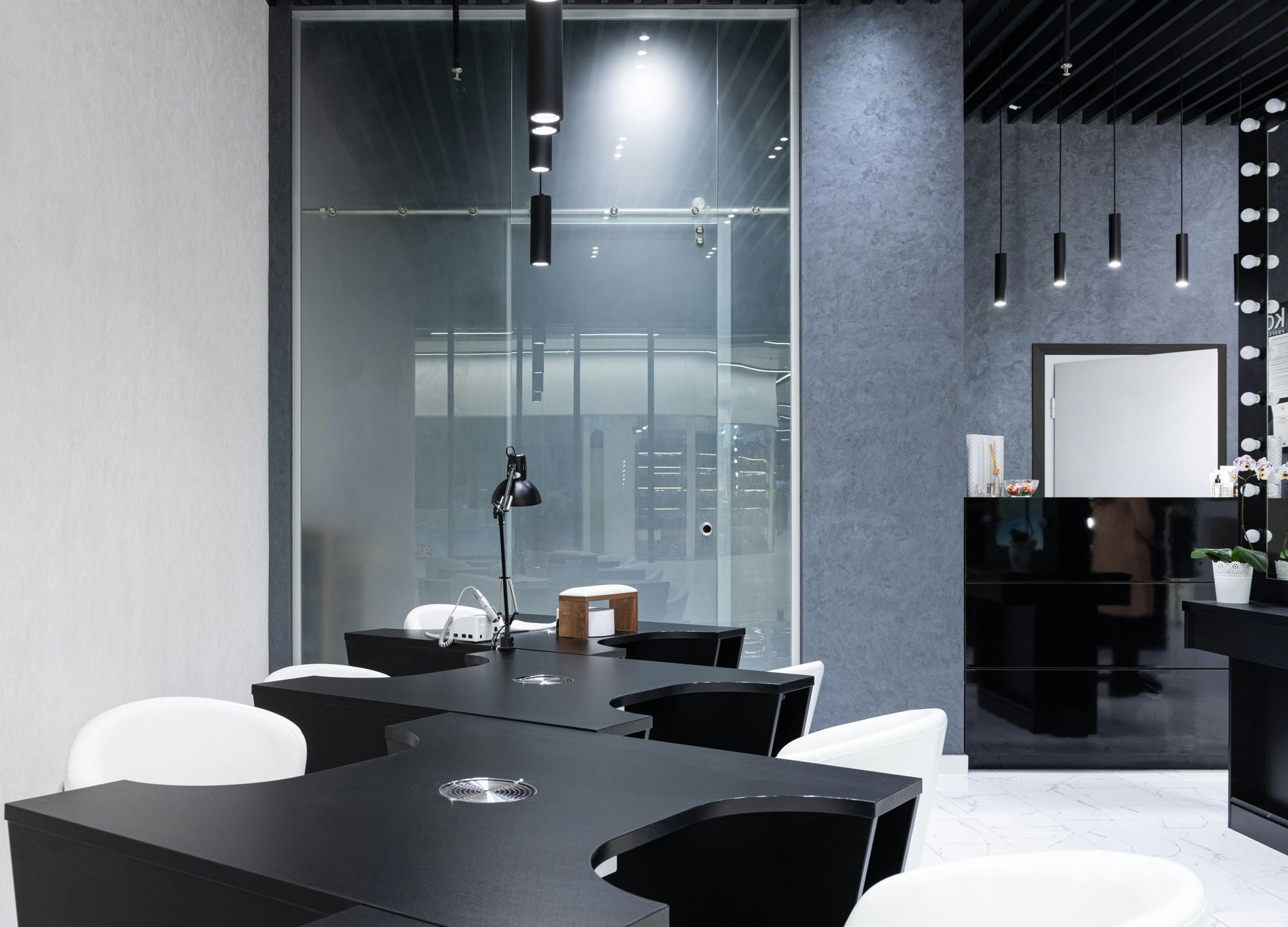 Modern salon interior with black and white furniture, glass partition, and pendant lighting.