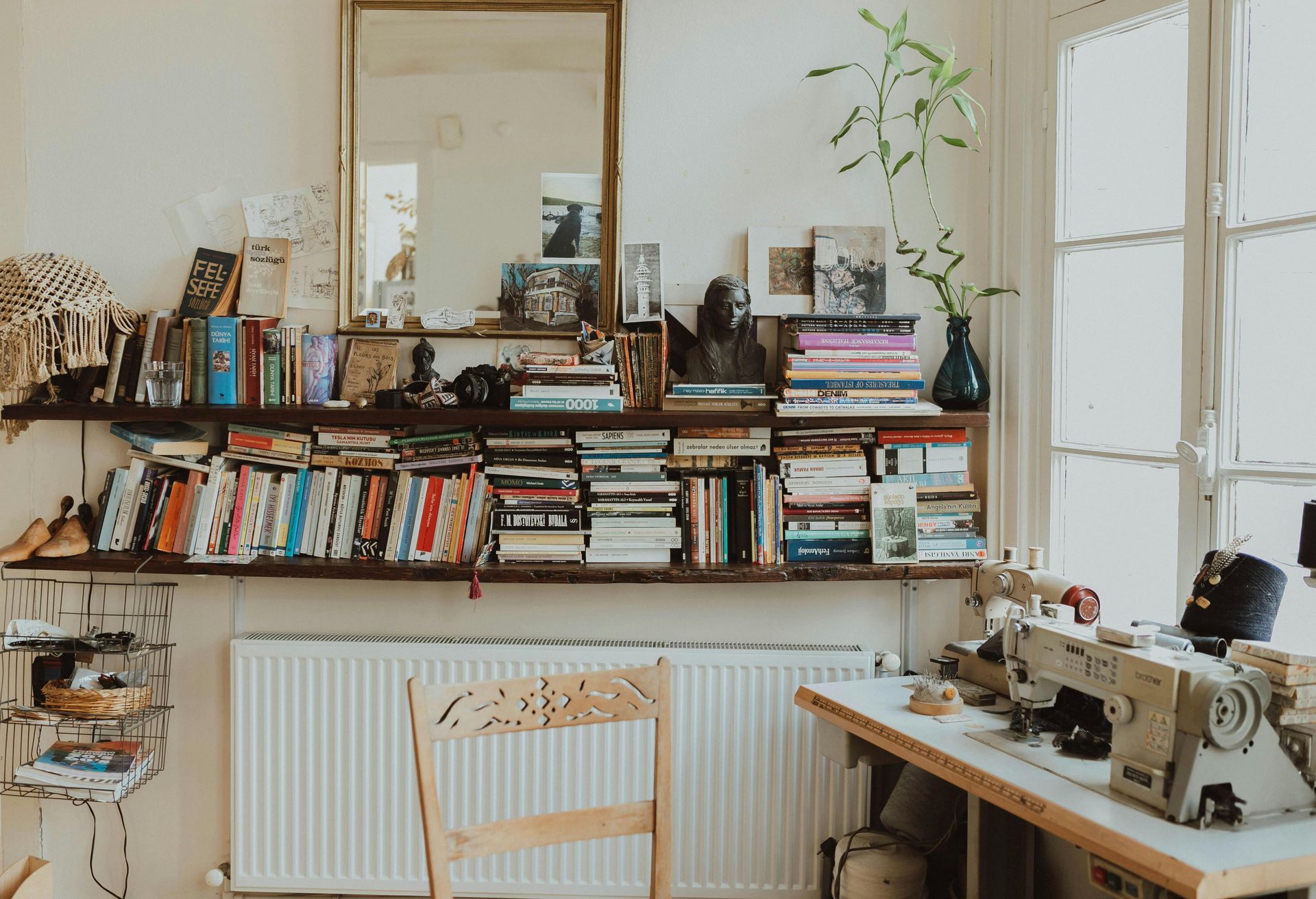 A cozy room with bookshelves, sewing machine, chair, and a window.