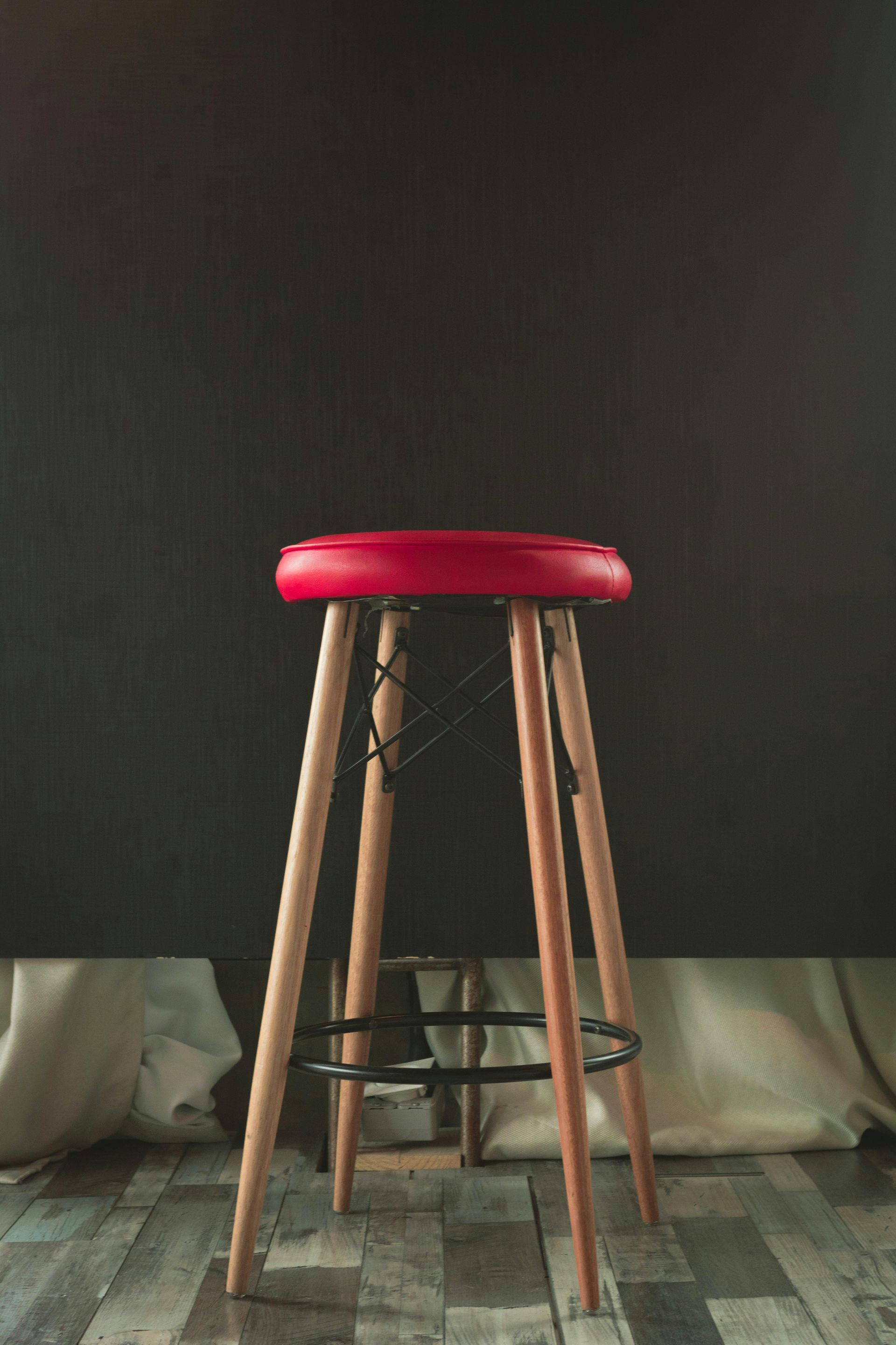 Red-topped bar stool with wooden legs against a dark gray backdrop and wooden floor.
