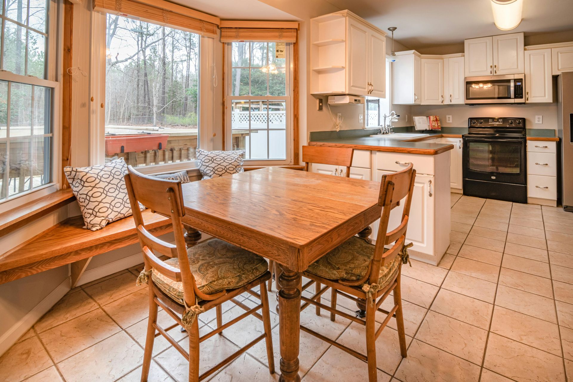 Kitchen with wood dining table, built-in window seat, white cabinets, and tile floor.