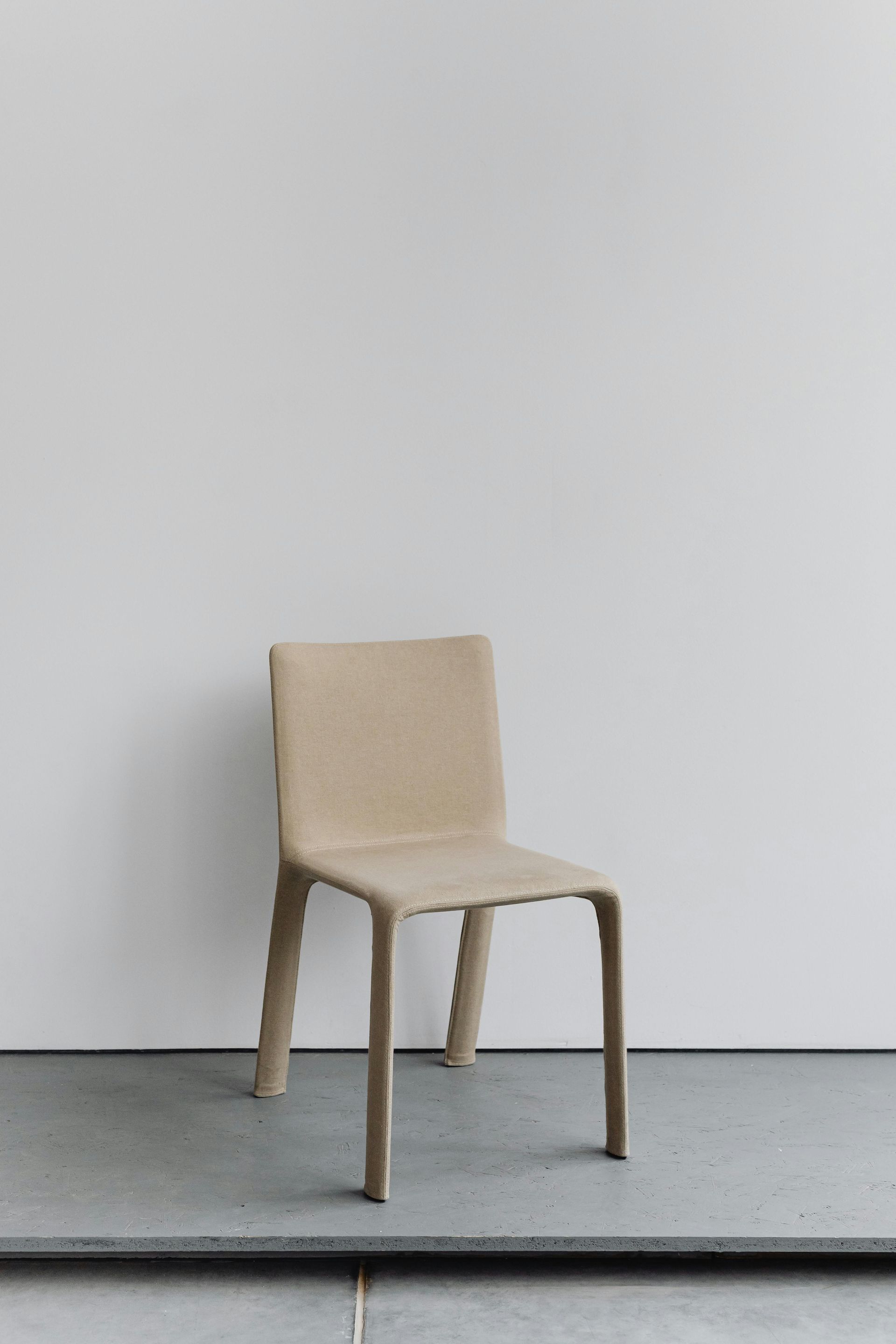 Beige chair against a white wall and a gray floor.