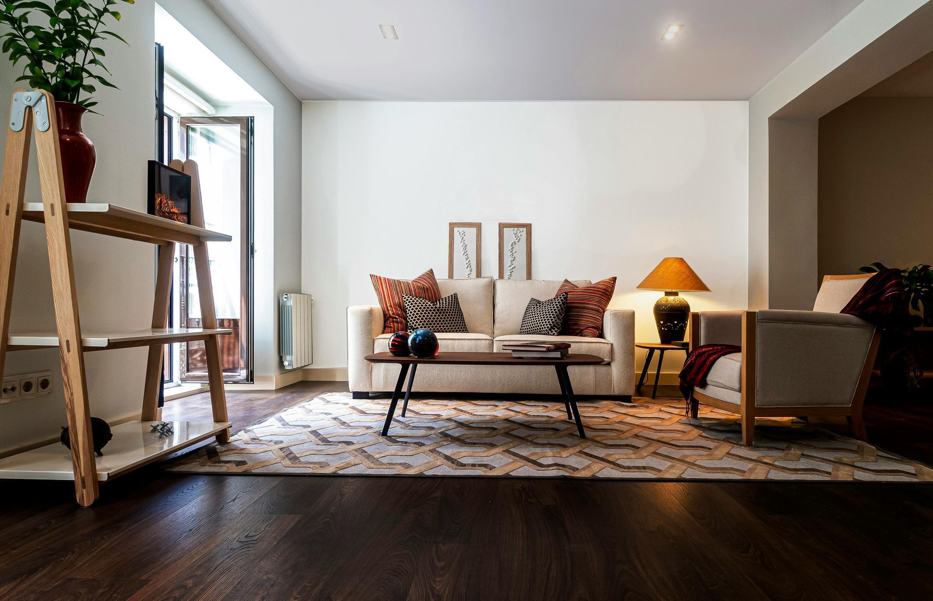 Living room with a white sofa, patterned rug, wooden shelves, and an open door.