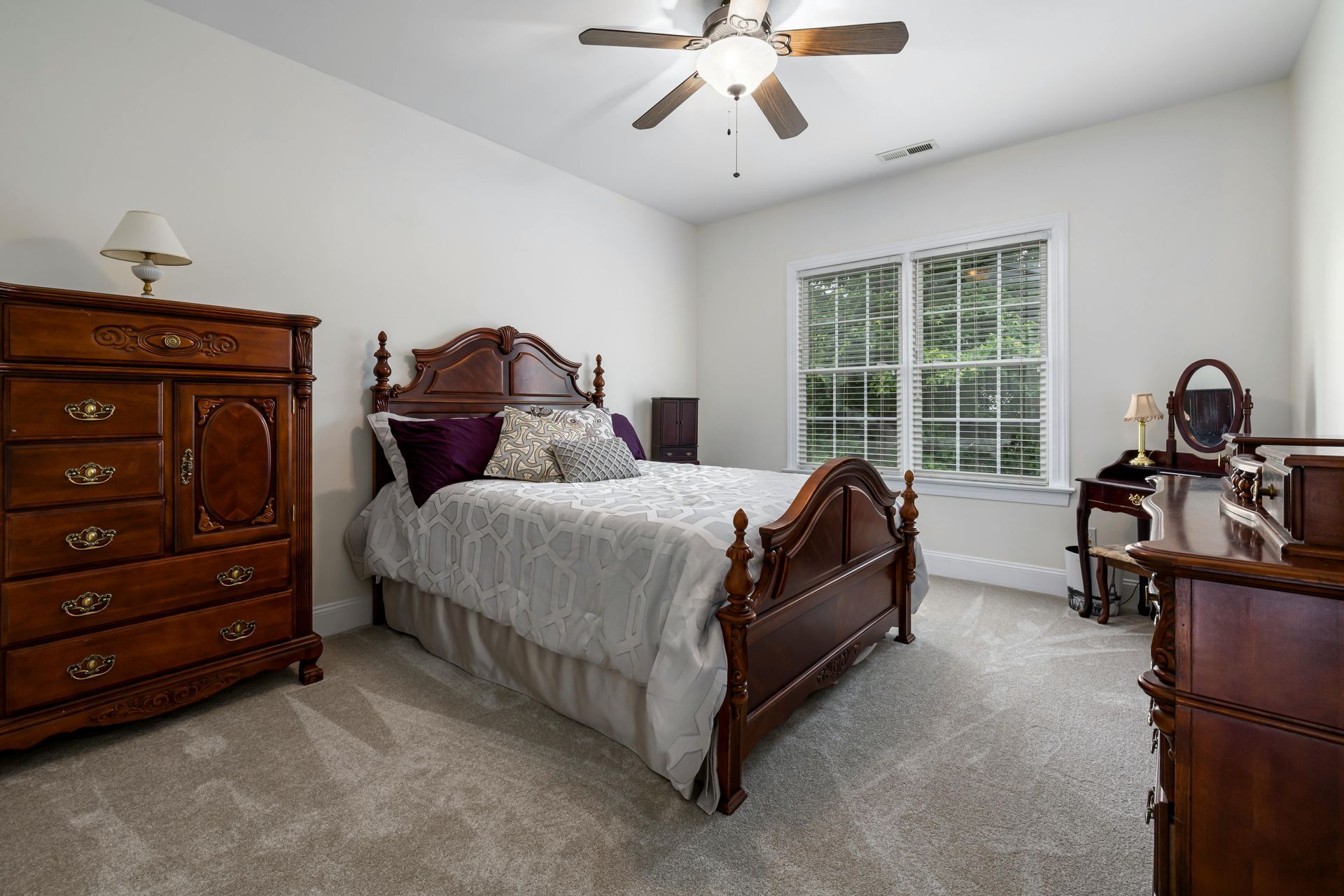 Bedroom with wooden furniture, bed with decorative headboard, window, and ceiling fan.