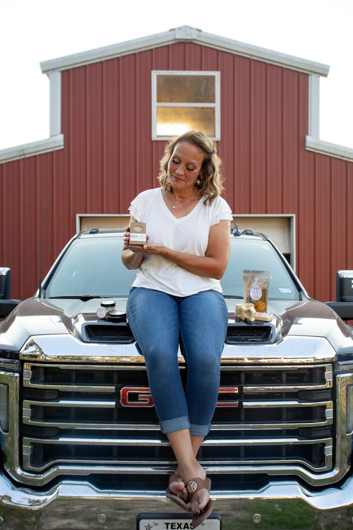Image of Robyn Holding a goats milk soap. Sitting on truck hood