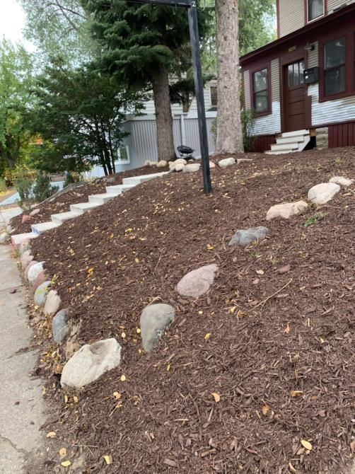 A well-manicured lawn bordered by natural rocks, featuring a rustic rock fire pit.