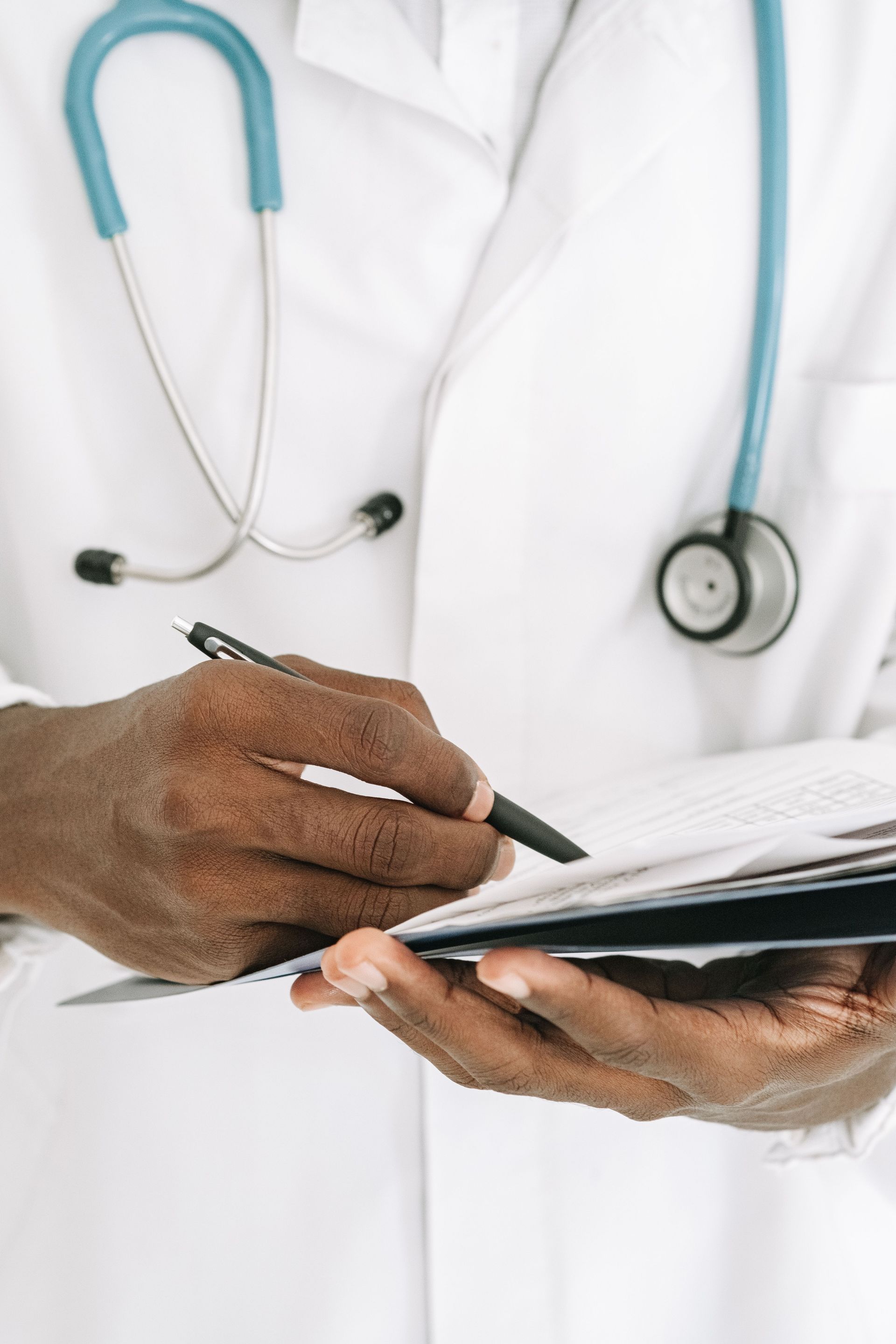 Doctor in white coat writing on a clipboard with a stethoscope around the neck