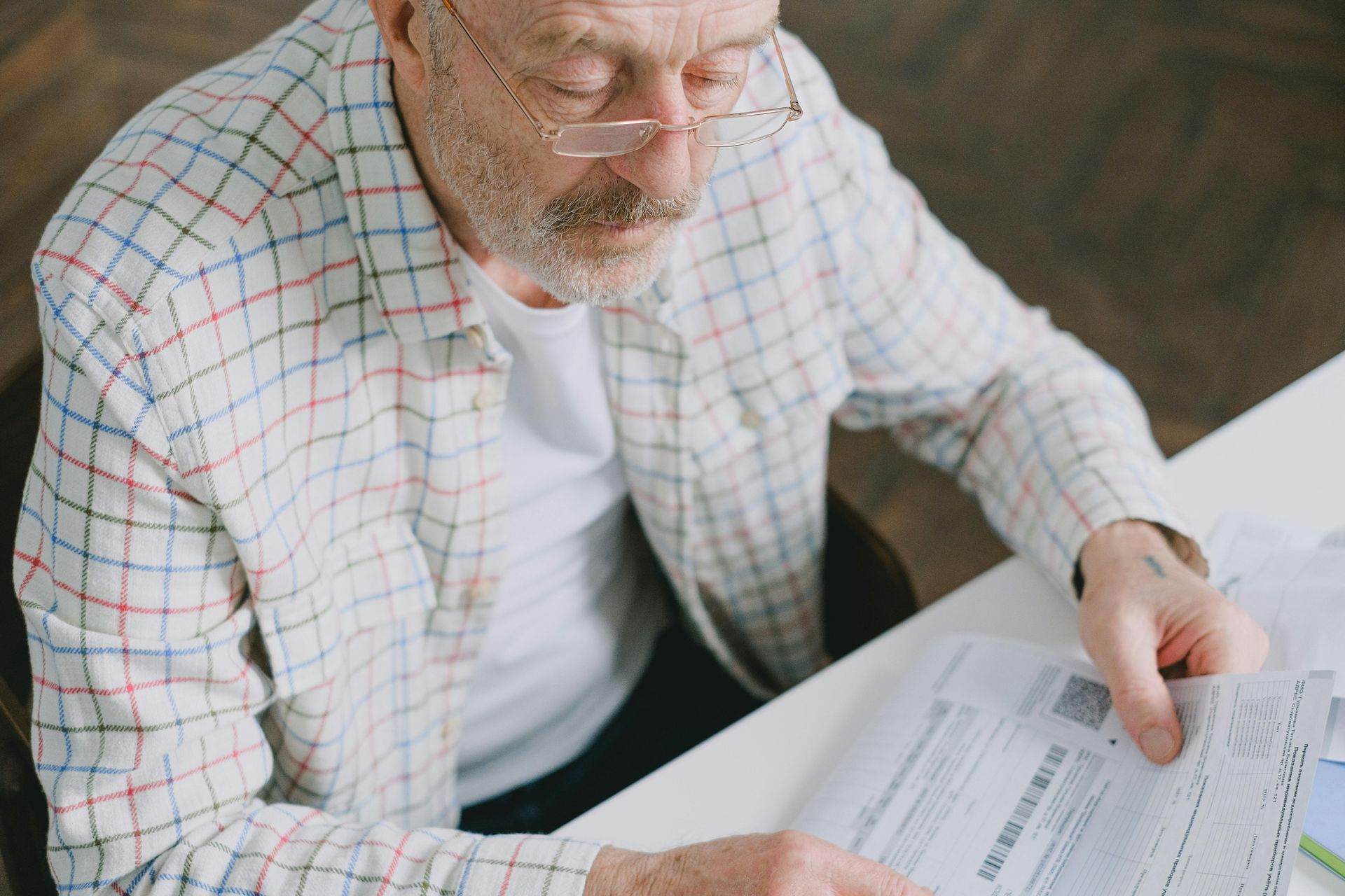 Man reviewing paperwork at a table, wearing glasses and a plaid shirt