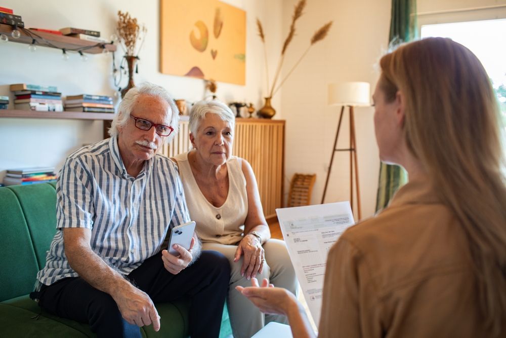 Counselor speaking with an elderly couple in a cozy living room, with papers in hand