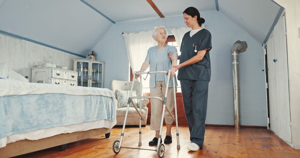 Caregiver assisting an elderly woman with a walker in a bright bedroom