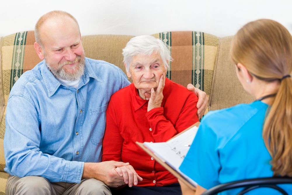 Caregiver talking with an elderly couple on a couch during a home visit