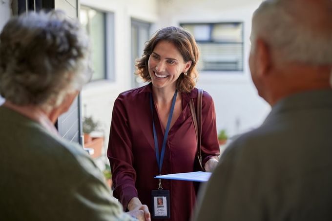 Smiling woman in a maroon blouse talking with two people outdoors near a building