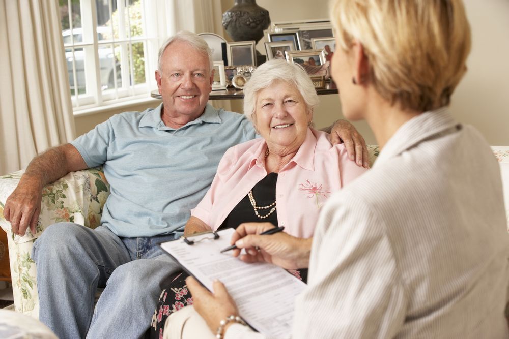 Older couple speaking with a counselor in a bright living room, seated on a sofa during a consultation.