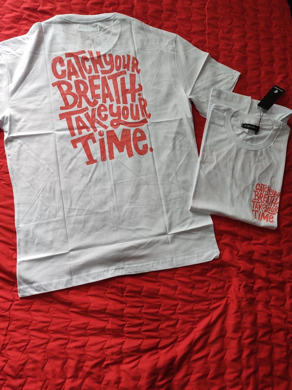 Dos camisetas blancas con texto rojo sobre una manta roja.