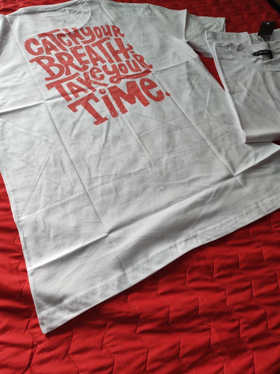 Dos camisetas blancas con texto rojo sobre una manta roja.
