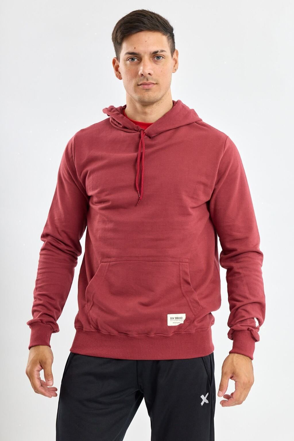 Un hombre lleva una sudadera con capucha roja y pantalones negros.
