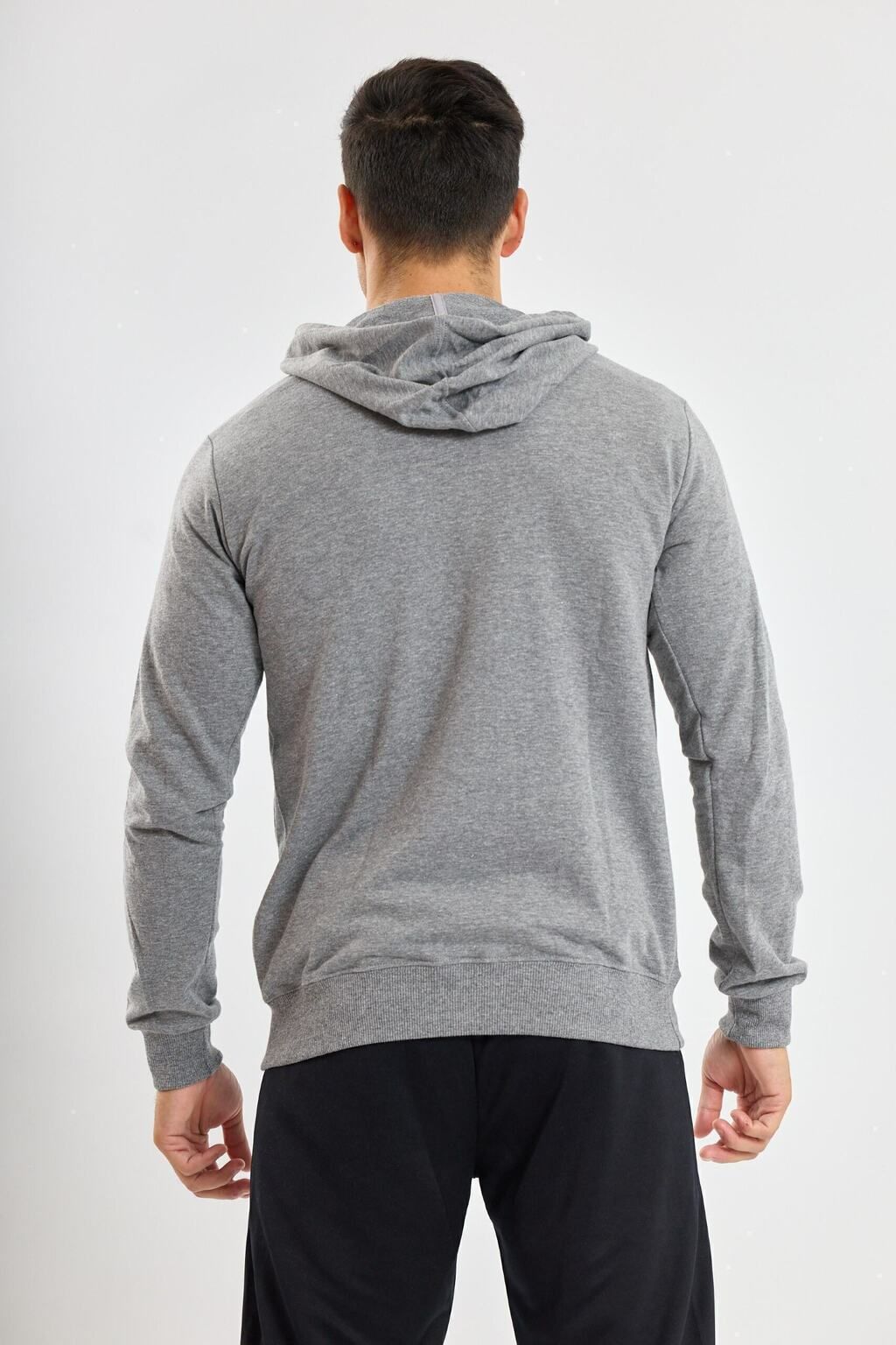 Un hombre lleva una sudadera con capucha gris y pantalones negros.