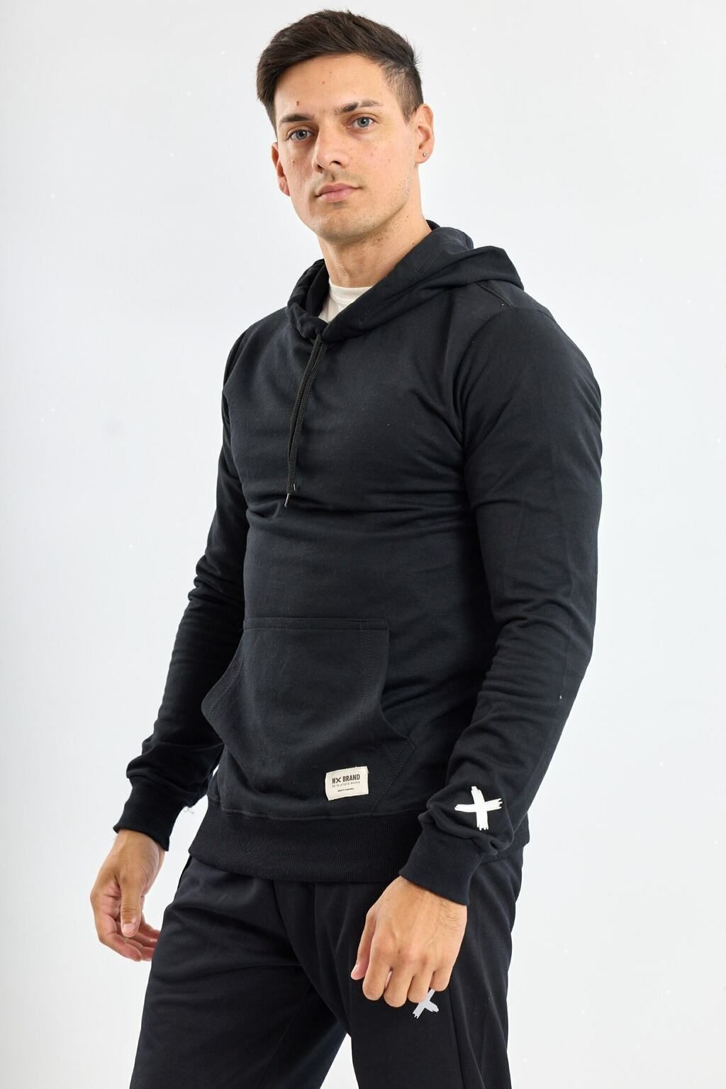 Un hombre lleva una sudadera con capucha negra y pantalones negros.