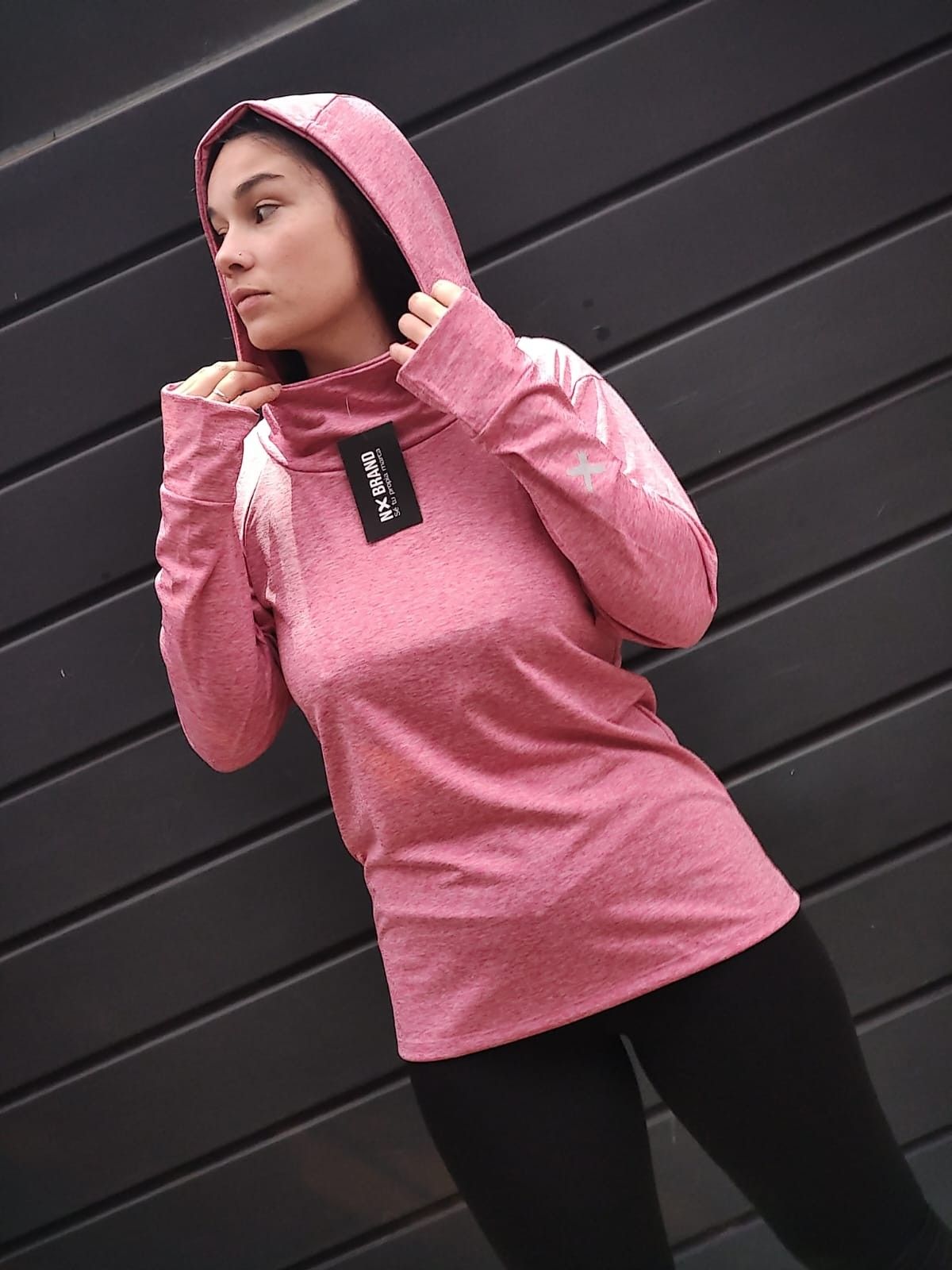 Una mujer que lleva una sudadera con capucha rosa está parada frente a una pared negra.
