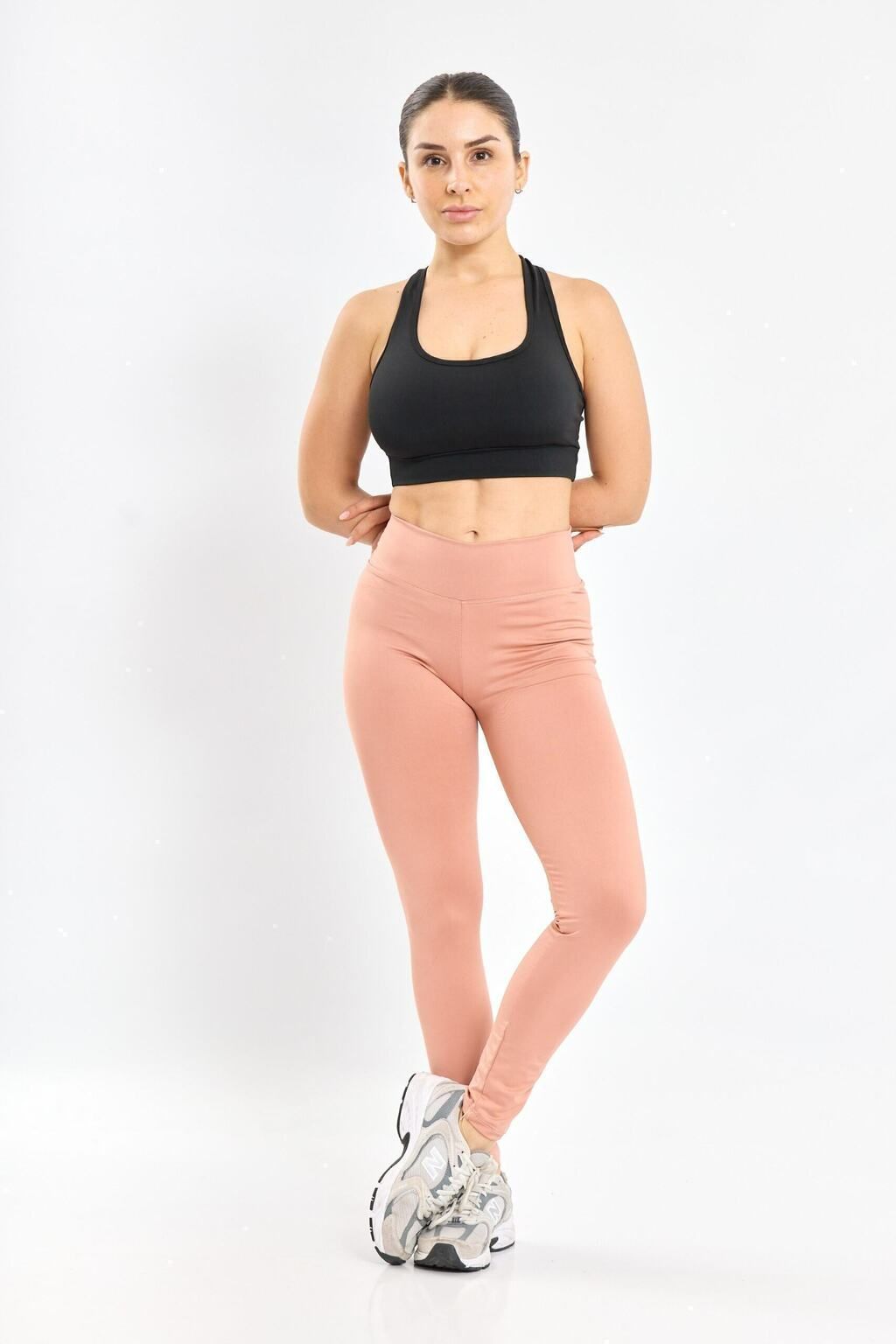 Una mujer lleva un sujetador deportivo negro y mallas marrones.