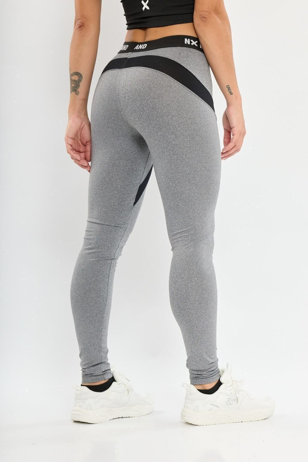 Una mujer lleva un par de leggings grises con rayas negras en los costados.