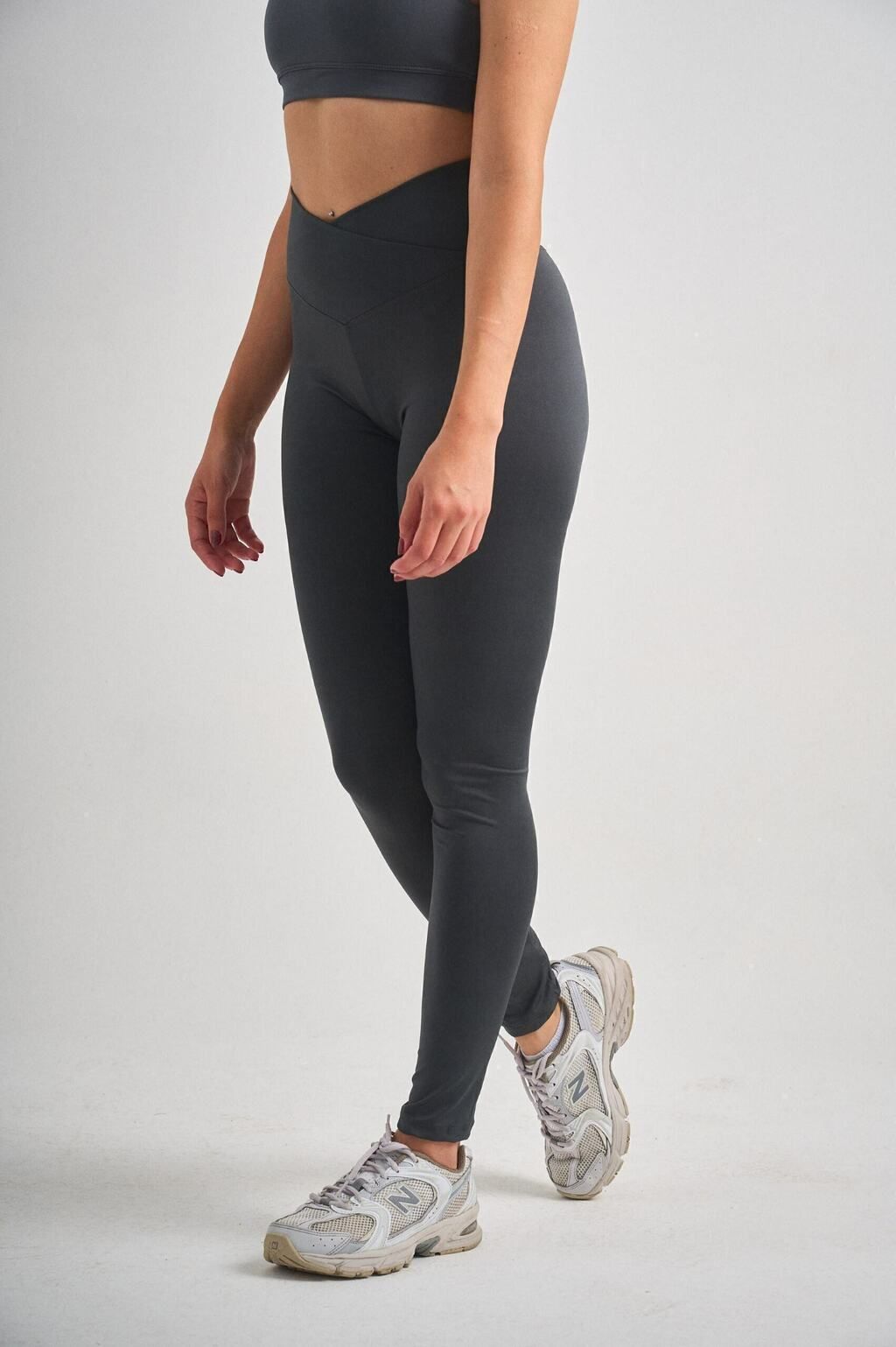 Una mujer que viste un top corto y leggings está de pie sobre un fondo blanco.