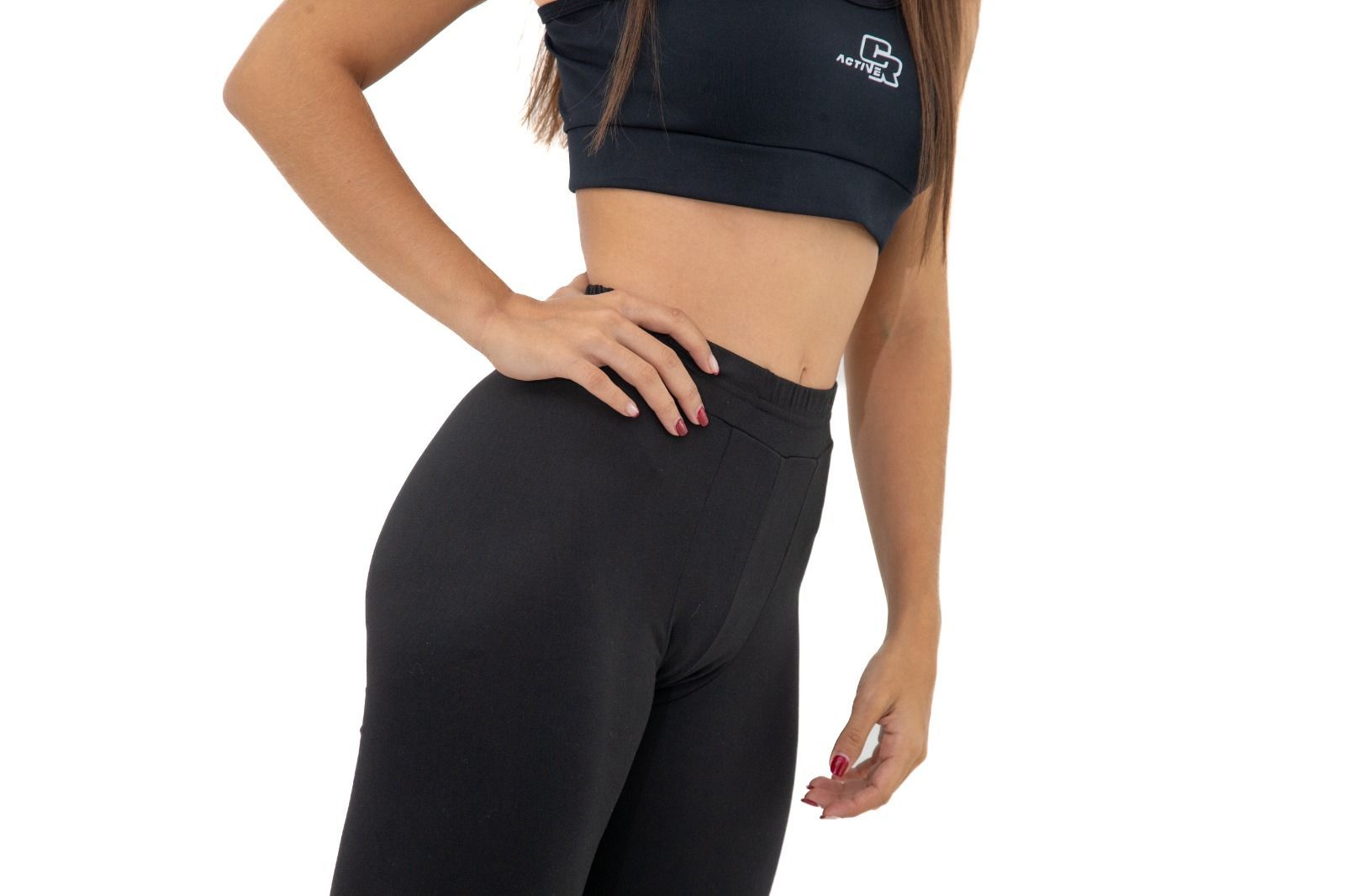 Una mujer con un top negro y leggings negros está de pie con las manos en las caderas.