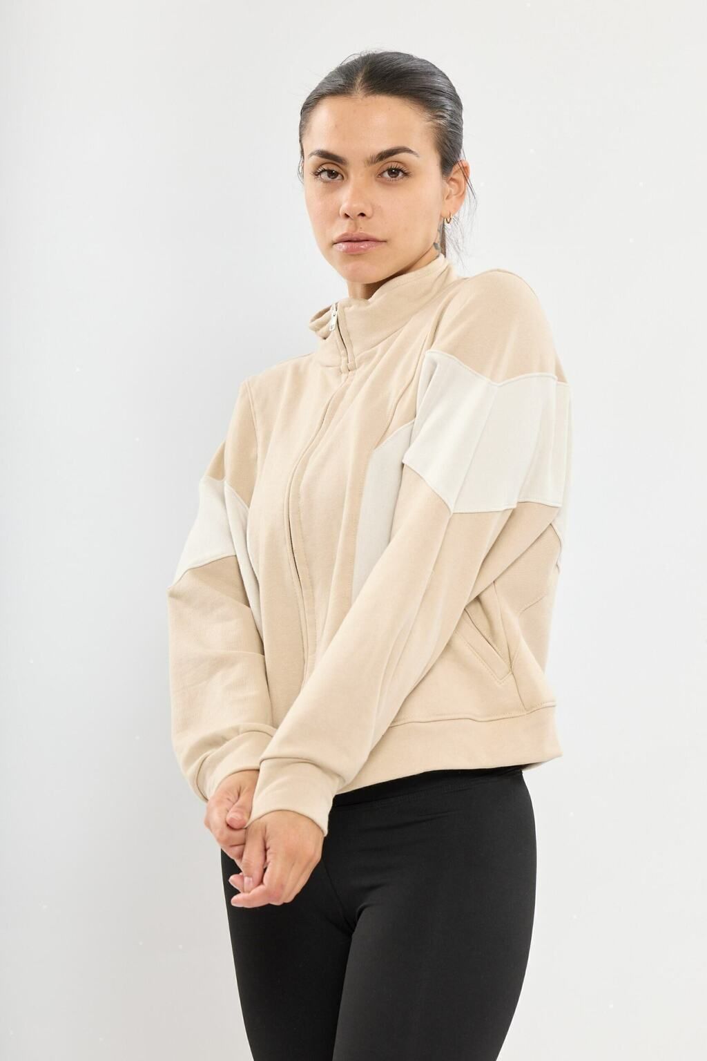 Una mujer lleva una sudadera beige y pantalones negros.
