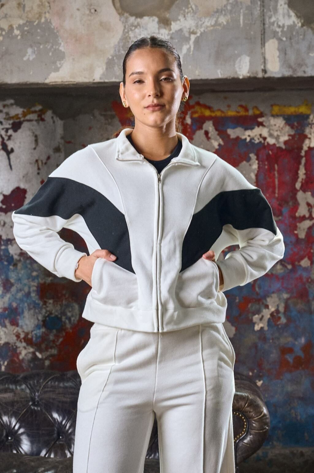 Una mujer que lleva una chaqueta blanca y pantalones blancos está parada frente a un sofá.