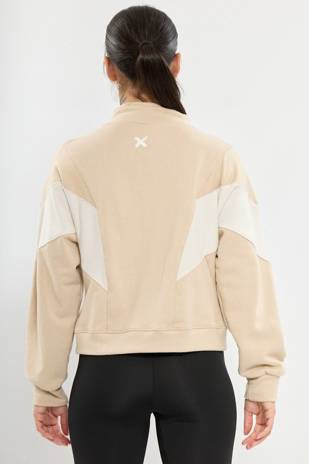 Una mujer lleva una sudadera beige y pantalones negros.