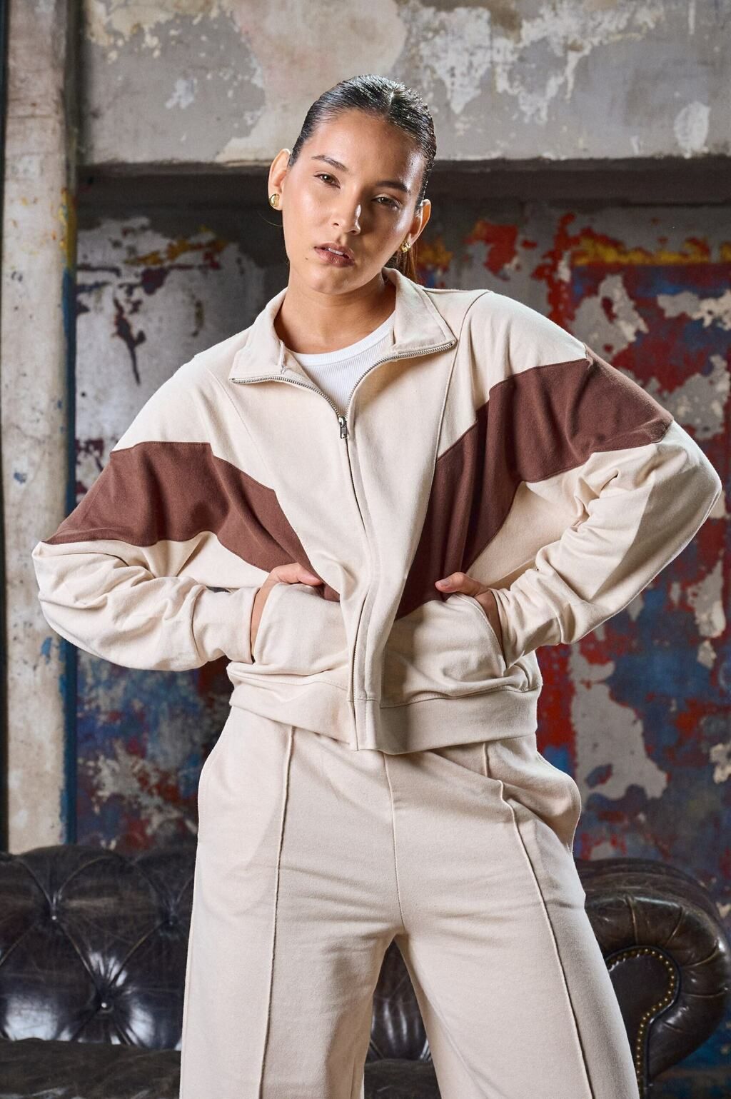 Una mujer con un chándal marrón y blanco está parada frente a una pared.