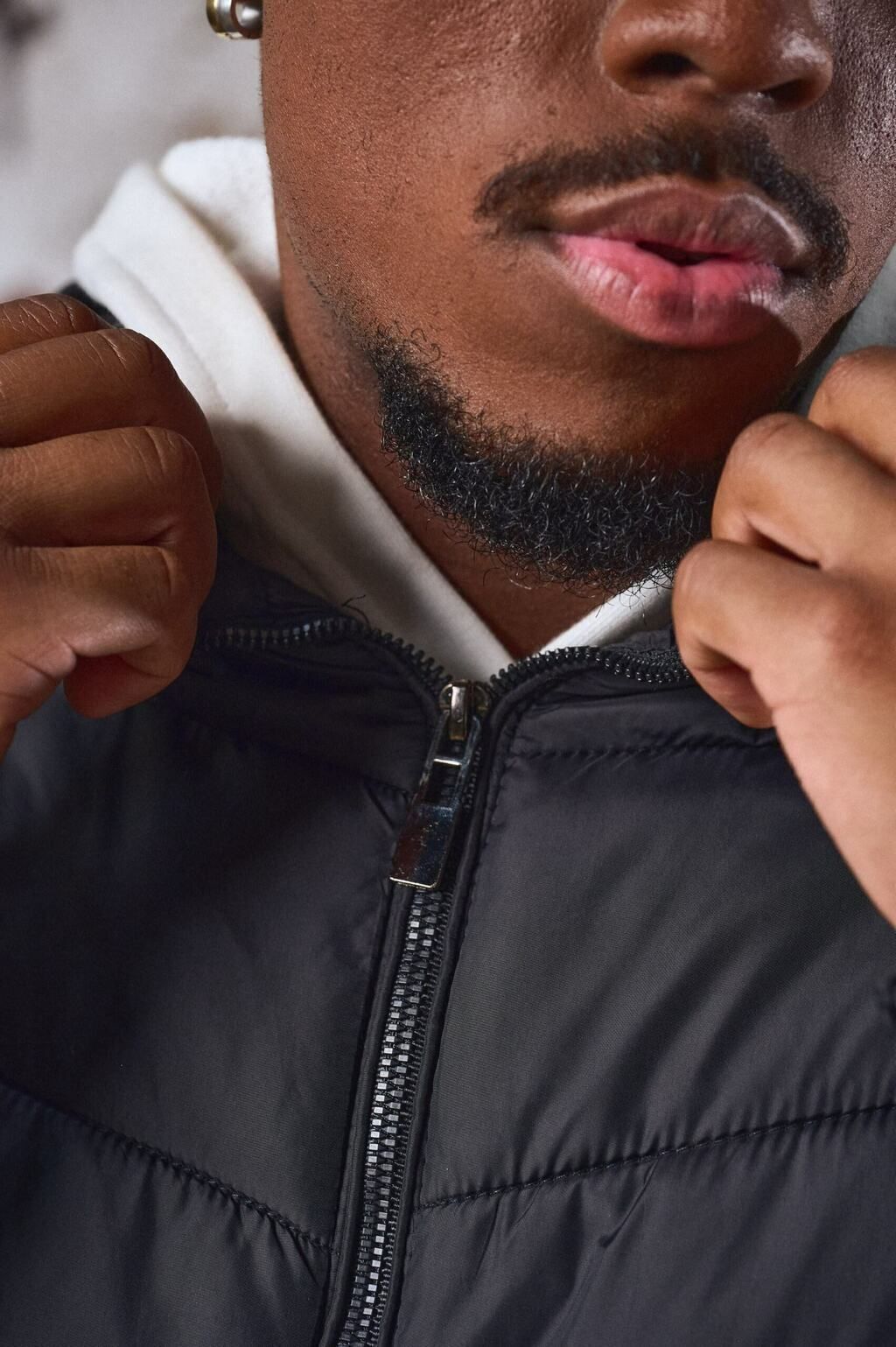 Un hombre que lleva una chaqueta negra y un cuello alto blanco está parado frente a una pared.