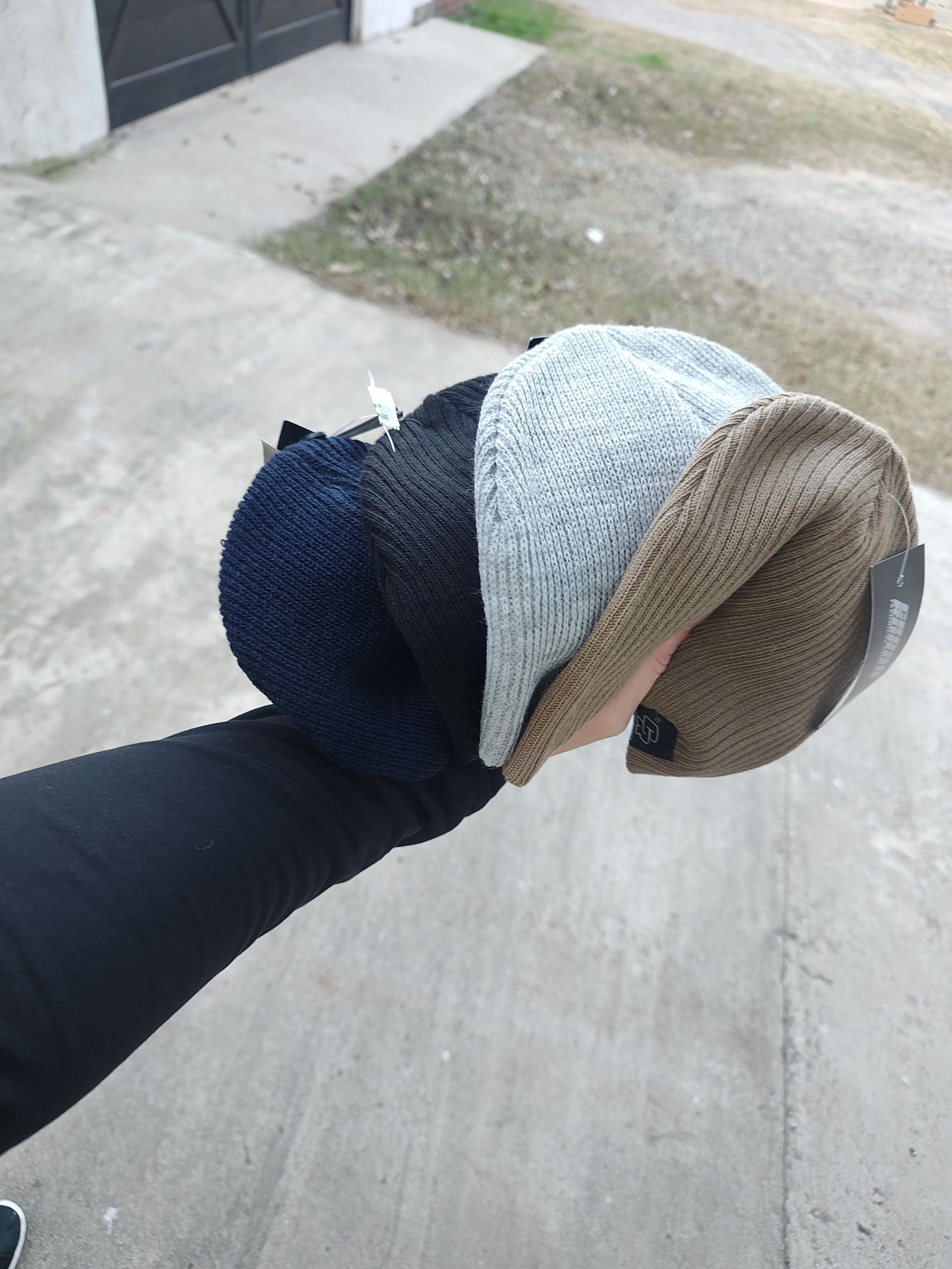 Hombre con gorro negro y camisa de manga larga, mirando a un lado. Al aire libre en la calle, con un coche al fondo.